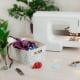 Light minimalist work space for tailor. White sewing machine and basket of sewing accessories on a table. Green house plants in seamstress working place. Concept of female small business at home.